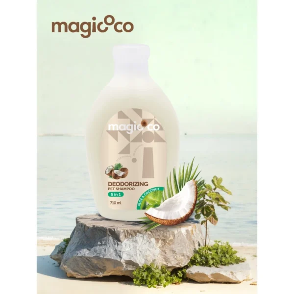White 710ml bottle of Magicoco 5-in-1 Deodorizing Pet Shampoo (Aloe & Coconut) placed on a rock near the ocean, with a fresh coconut slice and palm leaves nearby.