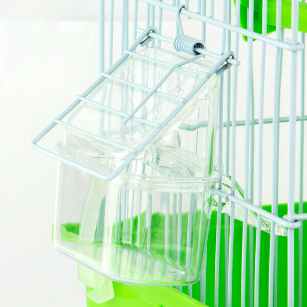 Zugo Outside Seed Feeder Cup, a clear plastic seed feeder with a hood, which is attached to the white wire side of a bird cage with a bright green base using light-colored wire clips.