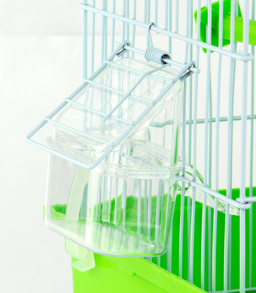 Zugo Outside Seed Feeder Cup, a clear plastic seed feeder with a hood, which is attached to the white wire side of a bird cage with a bright green base using light-colored wire clips.