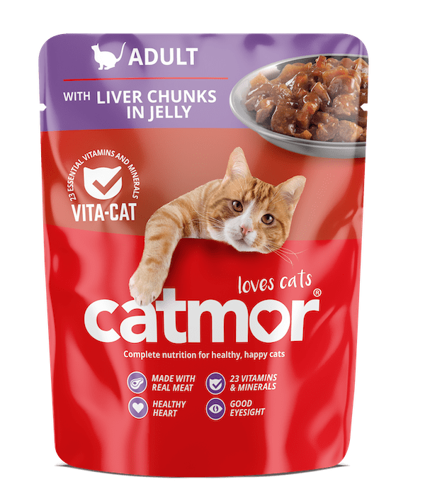 Product packaging for Catmor Adult Wet Cat Food, with a vibrant red and purple pouch design. The top purple section features a white cat silhouette and the word "ADULT" with the product description "WITH LIVER CHUNKS IN JELLY." A small bowl of the chunky, brown wet food is visible in the upper right corner. A ginger and white cat is shown playfully reaching its paw and head over the main red section, which displays the large white logo "catmor" and the slogan "loves cats." Key benefits are listed at the bottom with icons: "MADE WITH REAL MEAT," "23 VITAMINS & MINERALS," "HEALTHY HEART," and "GOOD EYESIGHT."