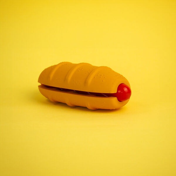 Hot Doggy Rubber Dog Toy, a hot dog-shaped toy with a textured orange bun and a red sausage.