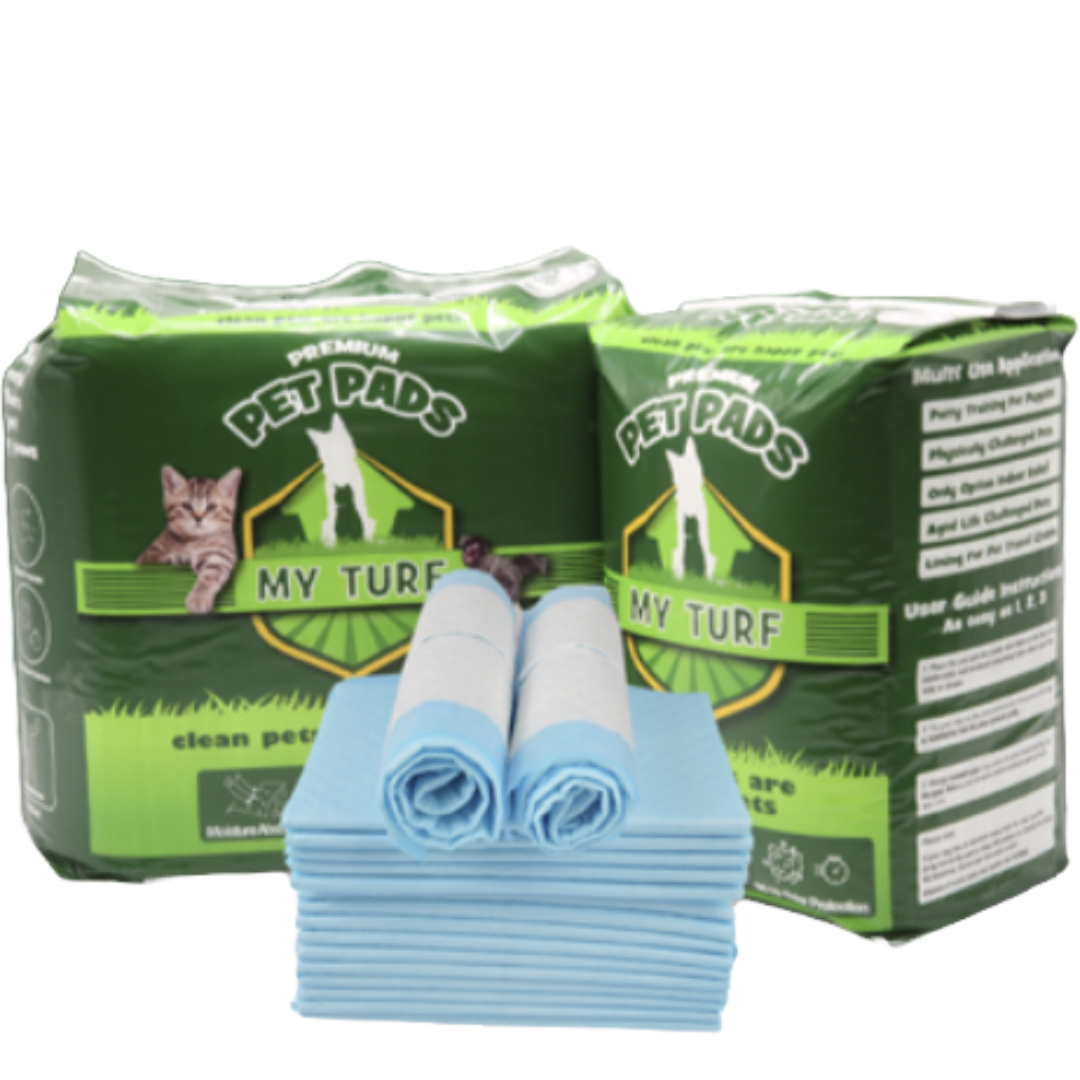 My Turf Premium Pet Pads (Twin Pack), two large green retail bags of MY TURF PREMIUM PET PADS flanking a stack of blue and white puppy training pads, with two pads rolled up on top of the stack.